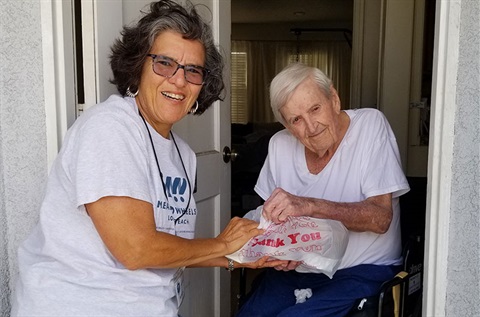 Meals on Wheels volunteer handing bag of food to woman in wheelchair