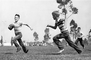 Boy running with football with other boys running behind (1956 photo)