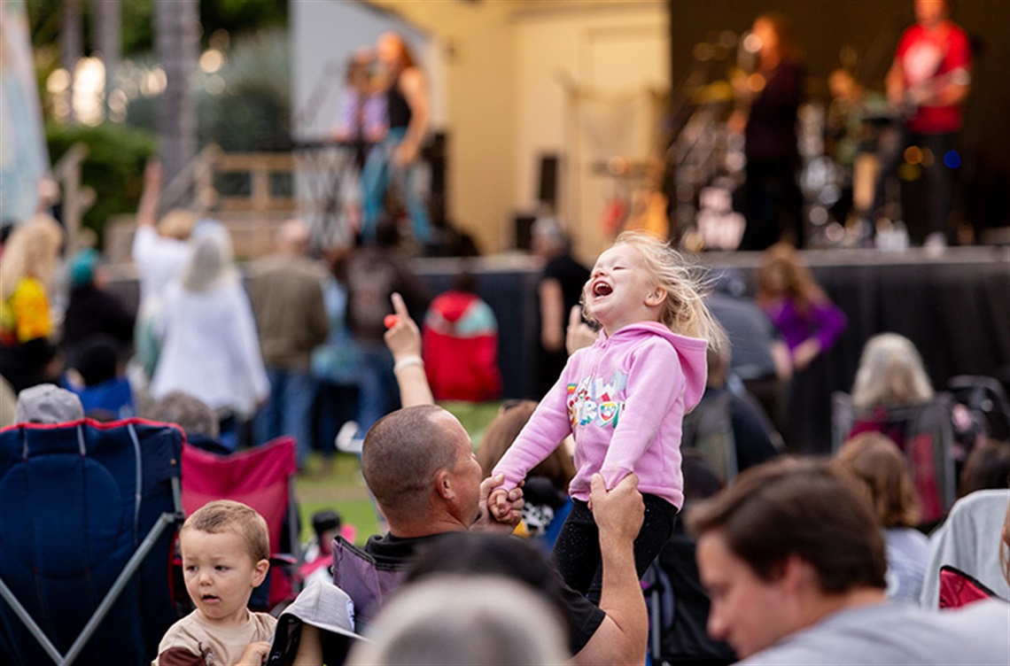 Happy little girl on dad's shoulders in front of band playing at park