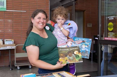 Mom holding child and book at book sale