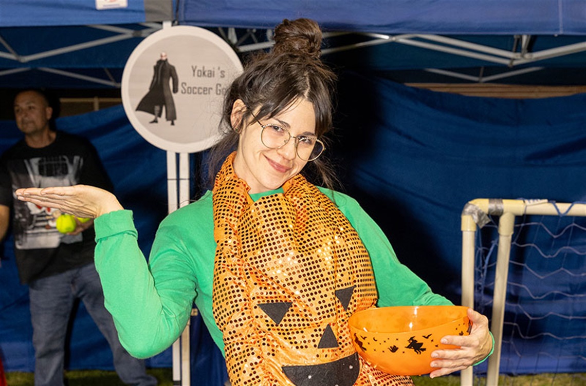 Smiling volunteer wears sequin pumpkin vest at Halloween carnival