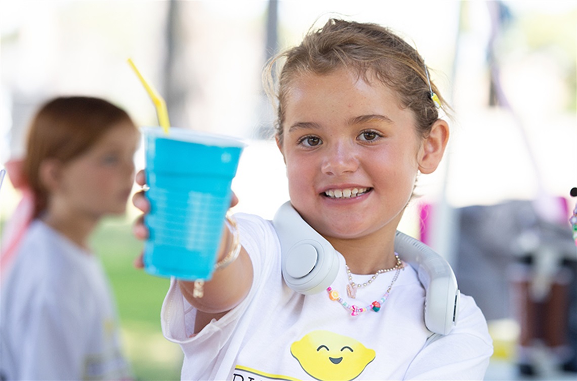 Smiling girl holds up a blue cup of lemonade